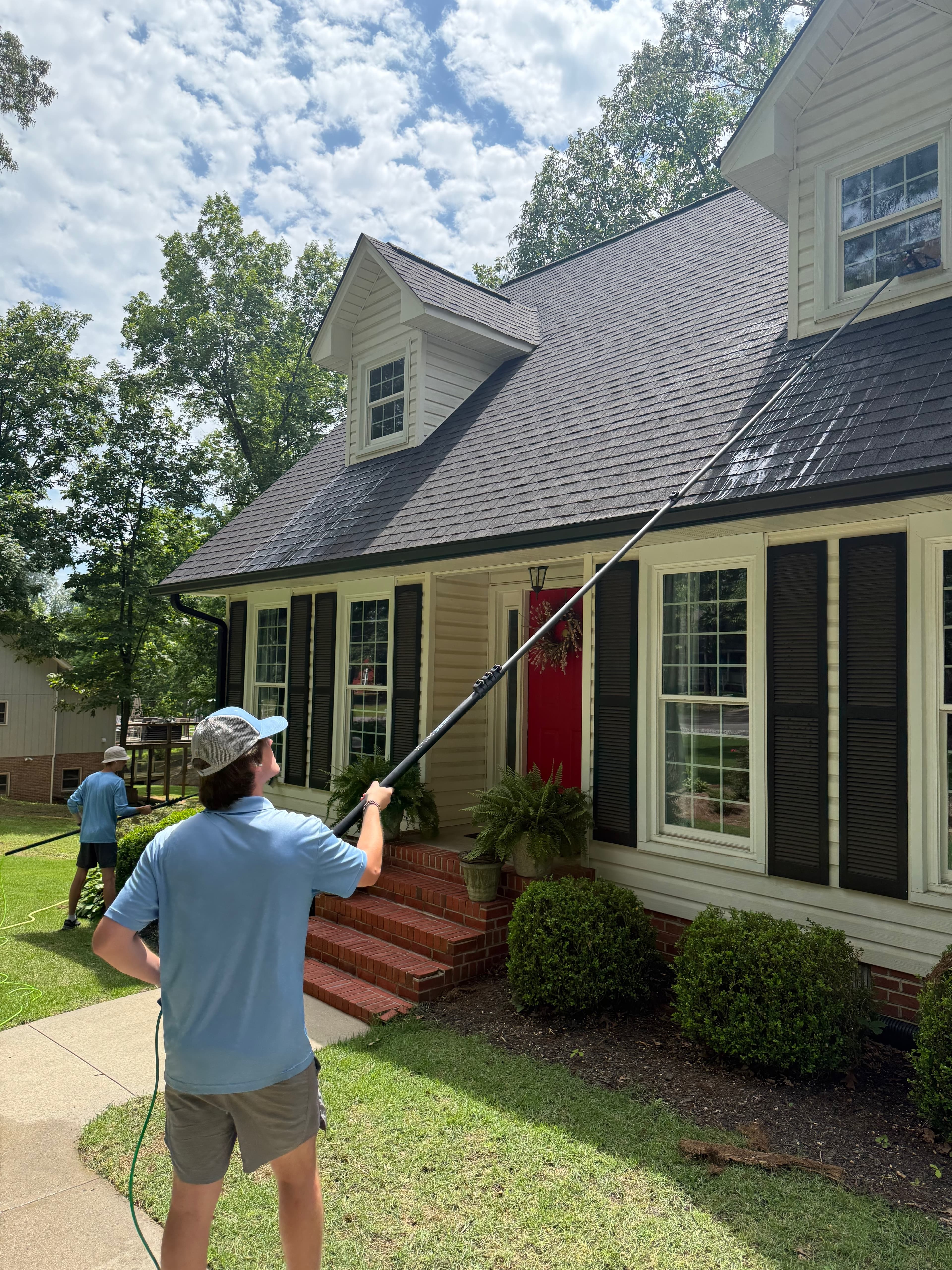 Man using a long extension pole to clean second-story windows of a white house.