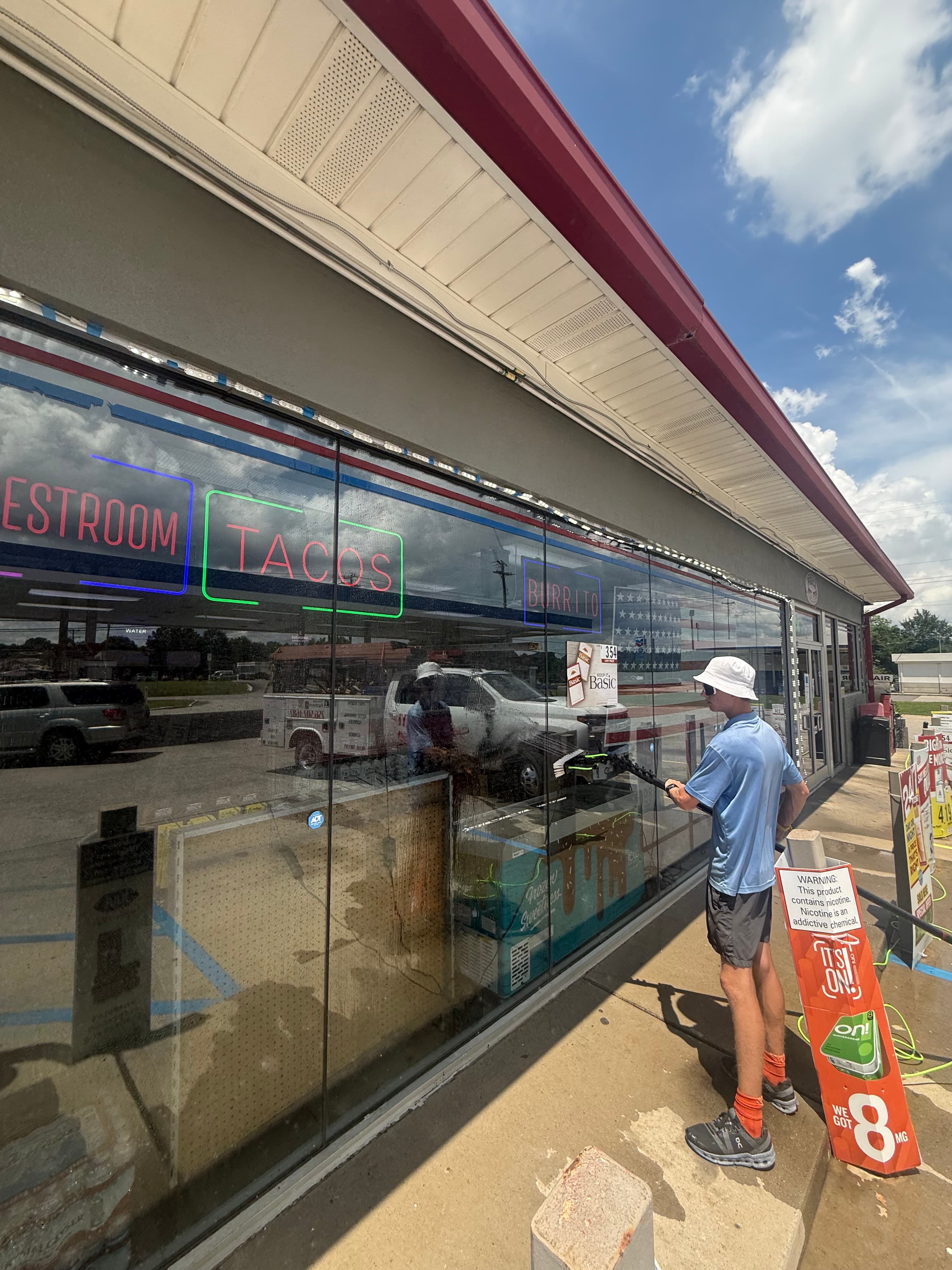 Man cleaning a storefront window featuring neon signs for restrooms, tacos, and burritos.