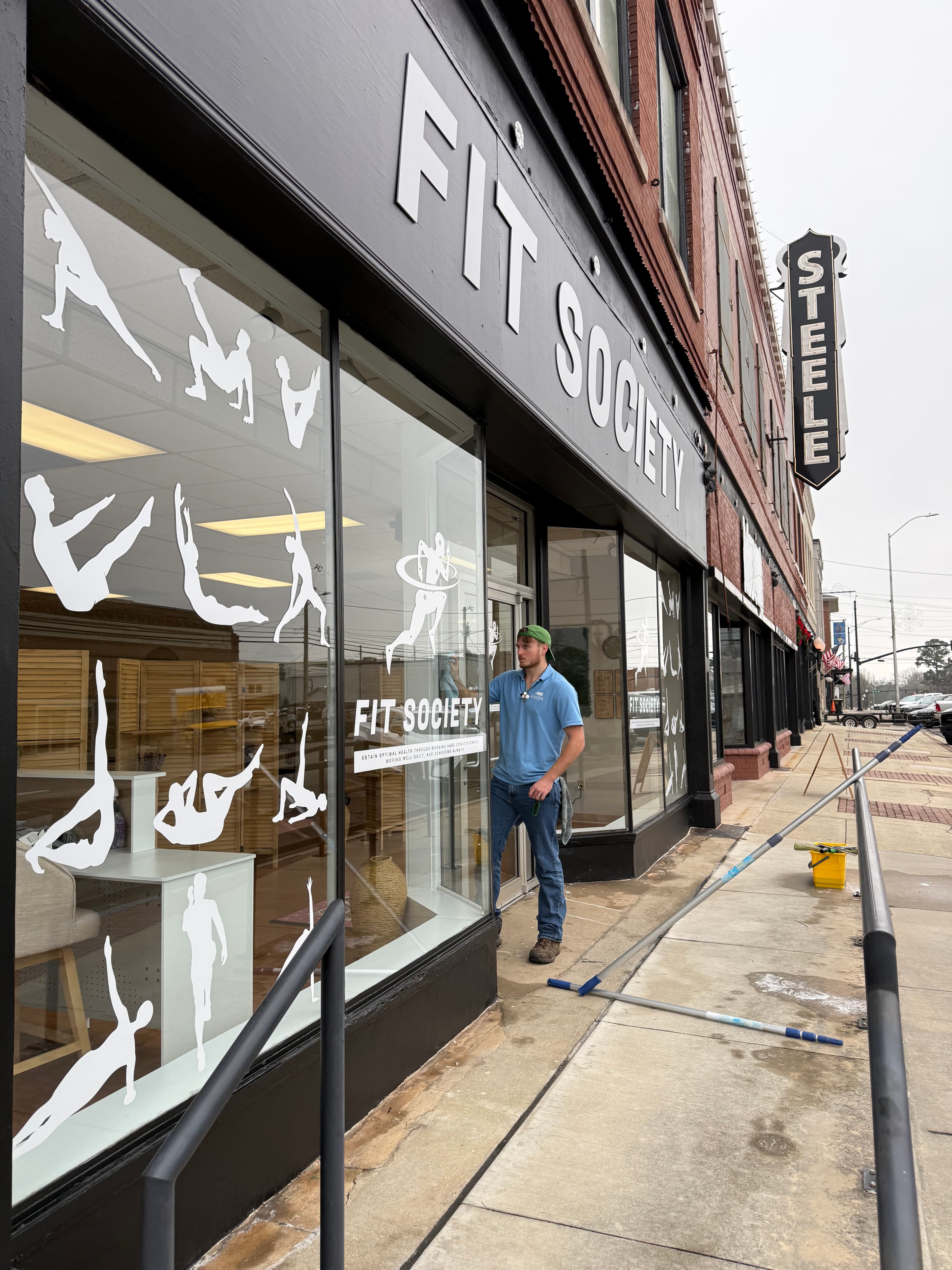 Man cleaning the windows of a Fit Society storefront with white athletic silhouette decals.