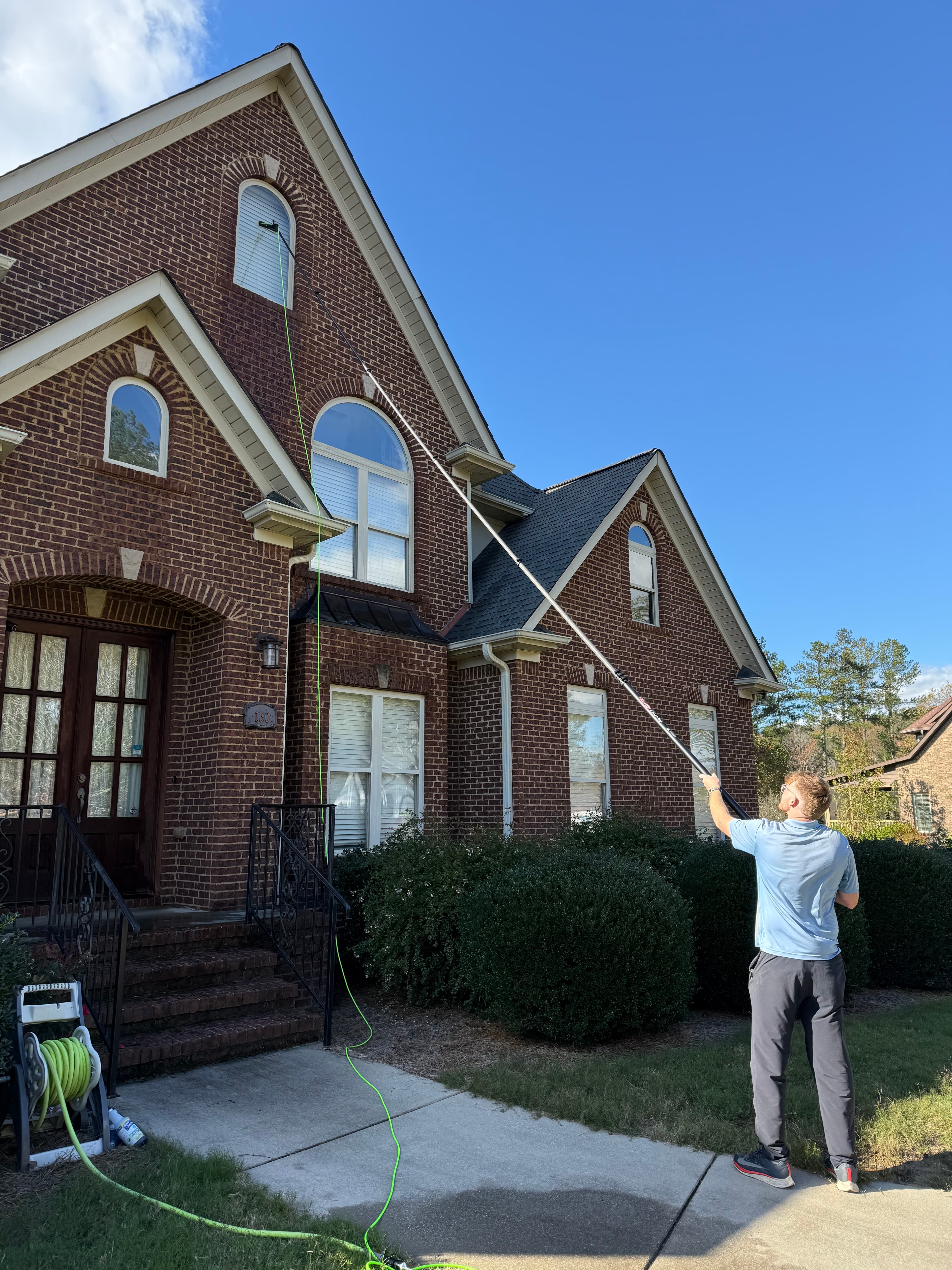 Man cleaning the high windows of a brick house with a long extension pole.