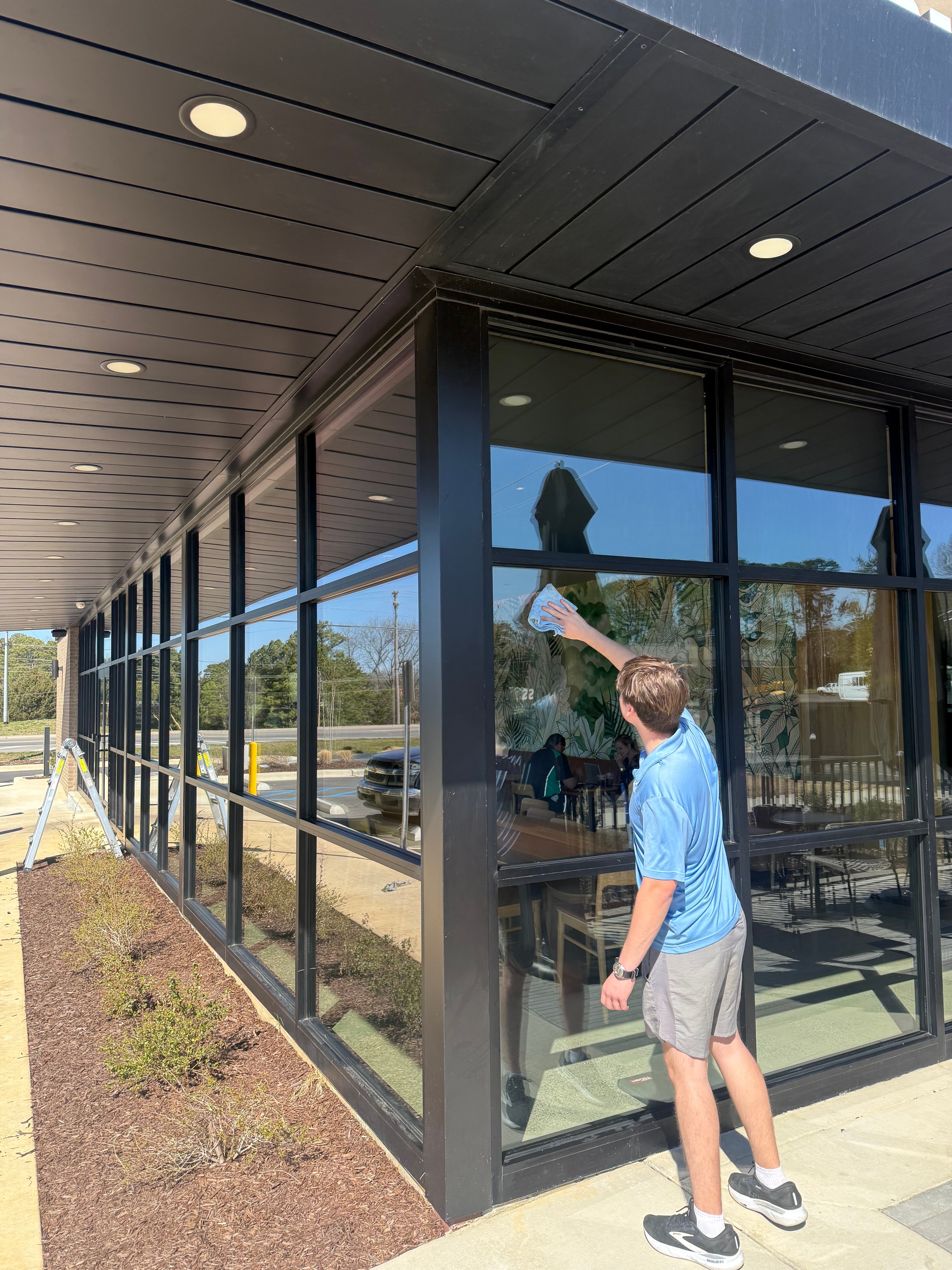 Man in blue shirt cleaning large glass window of a modern building with a cloth.